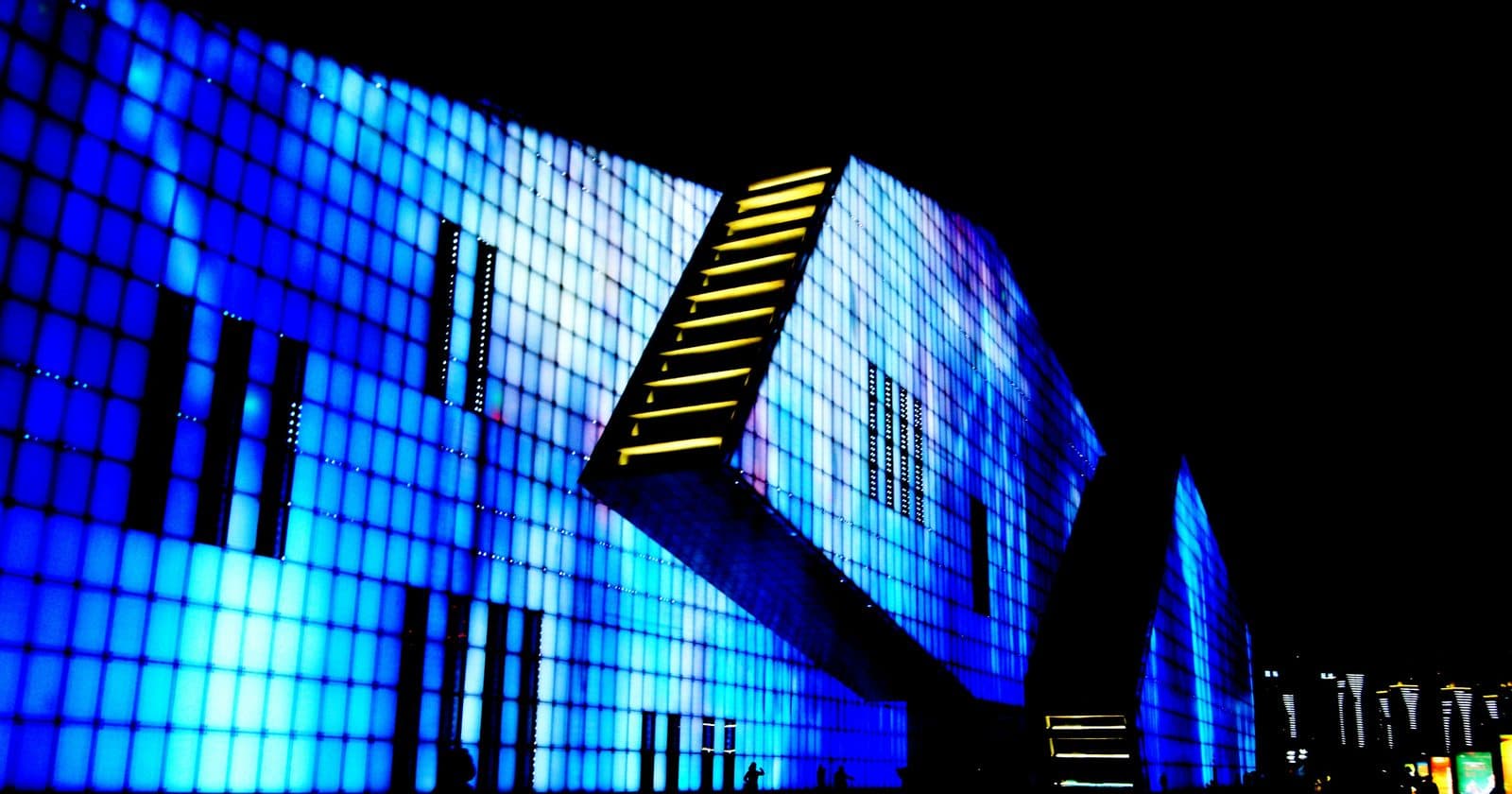 A large blue-lit LED facade wrapping the side of a building at night