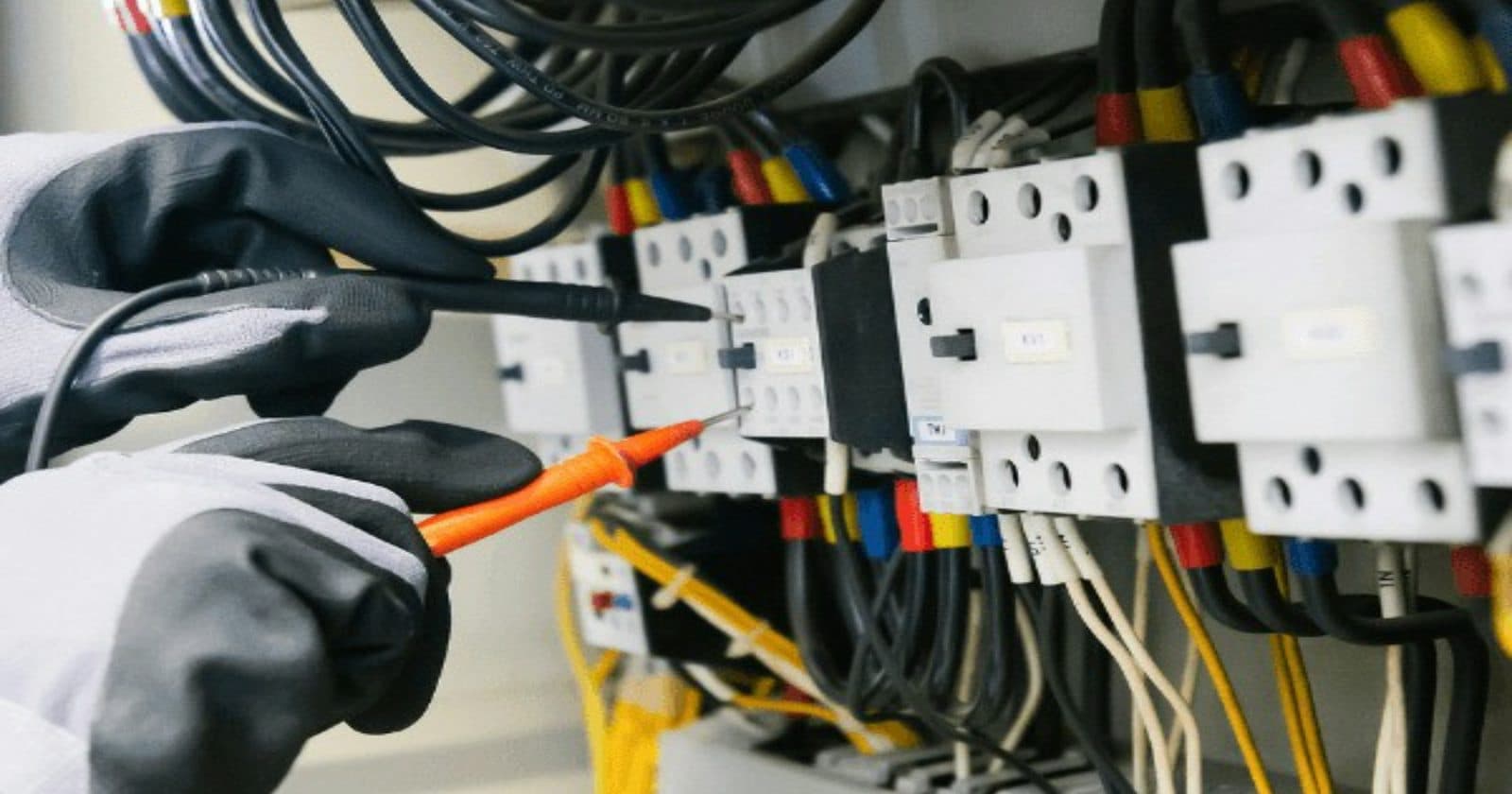 A gloved electrician testing a distribution board with a multimeter